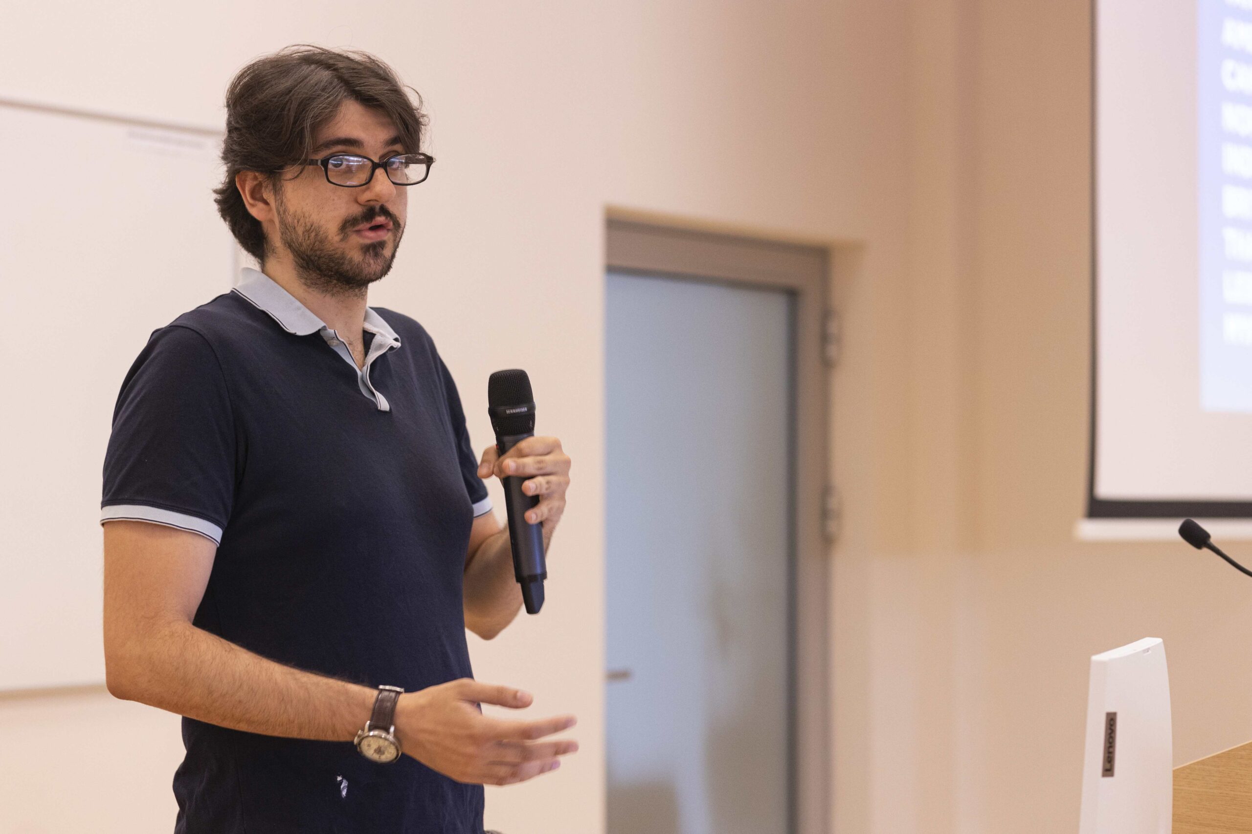 A man in glasses gives a presentation in front of a screen, illustrating his ideas and engaging the audience.