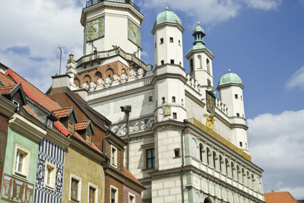 A striking image of an ornate, historical building with a colorful facade and multiple towers, possibly a town hall or significant cultural landmark. The architecture features intricate designs, with other vibrant buildings visible alongside it, suggesting this is in a well-preserved historical district.