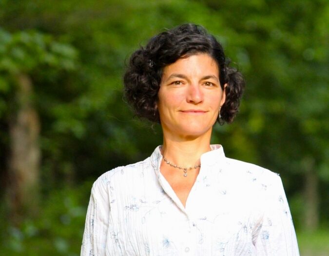 Jennifer Baker-Porazinski, M.D. A woman with short hair stands confidently in front of a backdrop of lush green trees, embodying a serene outdoor moment.