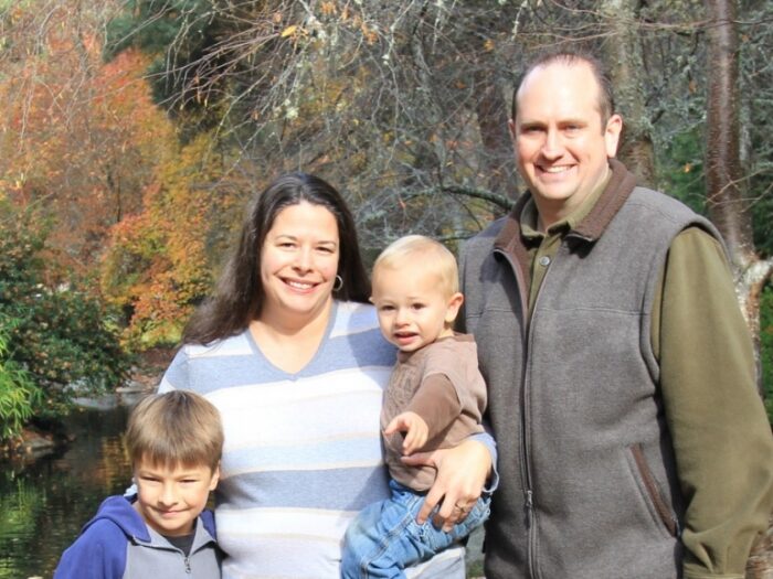 Jacqueline Wilk, M.D A family stands together smiling in front of a serene pond, capturing a joyful moment in nature.