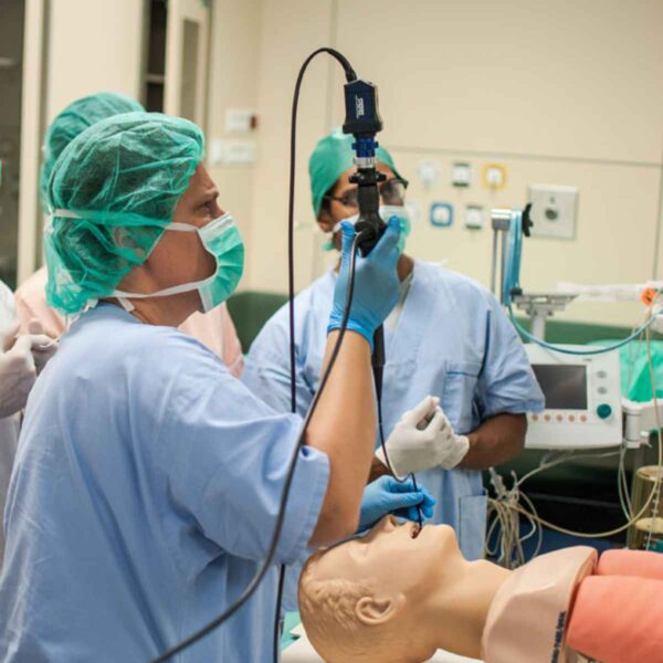 A team of medical professionals in scrubs practicing procedures on a training dummy in a clinical setting.
