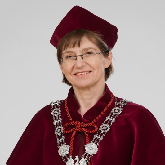 A woman in a burgundy academic robe and hat, wearing glasses, exudes calm dignity with silver chain regalia and a medallion.
