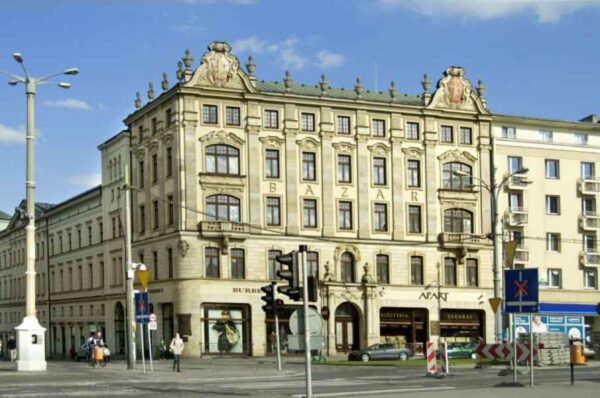 An elegant, historic building with detailed stone carvings and large windows. The word "BAZAR" is prominently displayed at the top, suggesting a commercial or significant historical site. The building is situated at a busy intersection, adding to its prominence in the area.