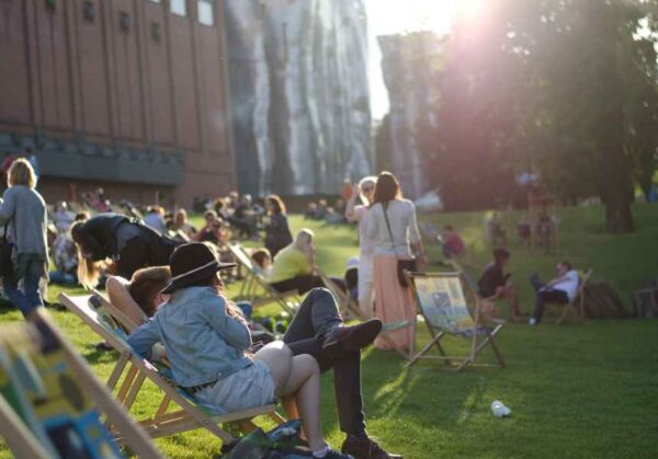 People relaxing on sun chairs at an outdoor event, enjoying a sunny day in an open green space.