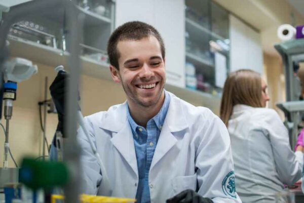 A cheerful man wearing a lab coat holds a test tube, representing a positive approach to scientific research and experimentation.